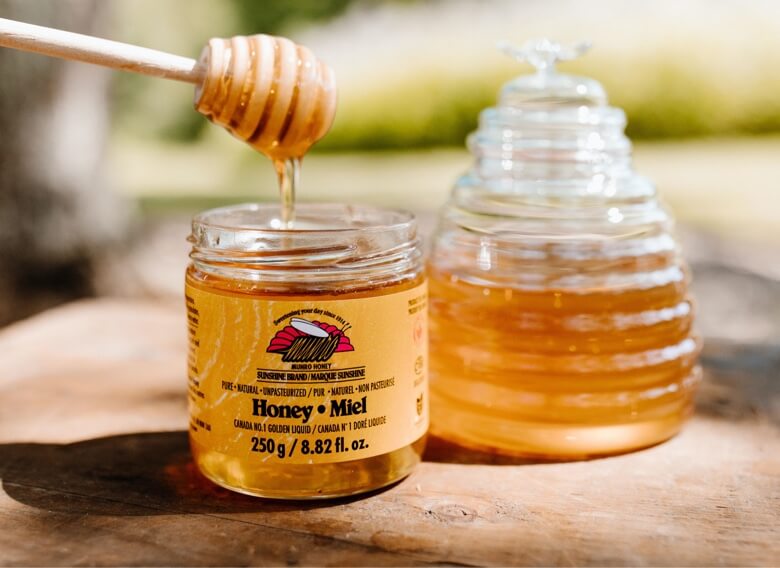 Munro Honey branded honey pot with honey dripping from wooden honey dripper